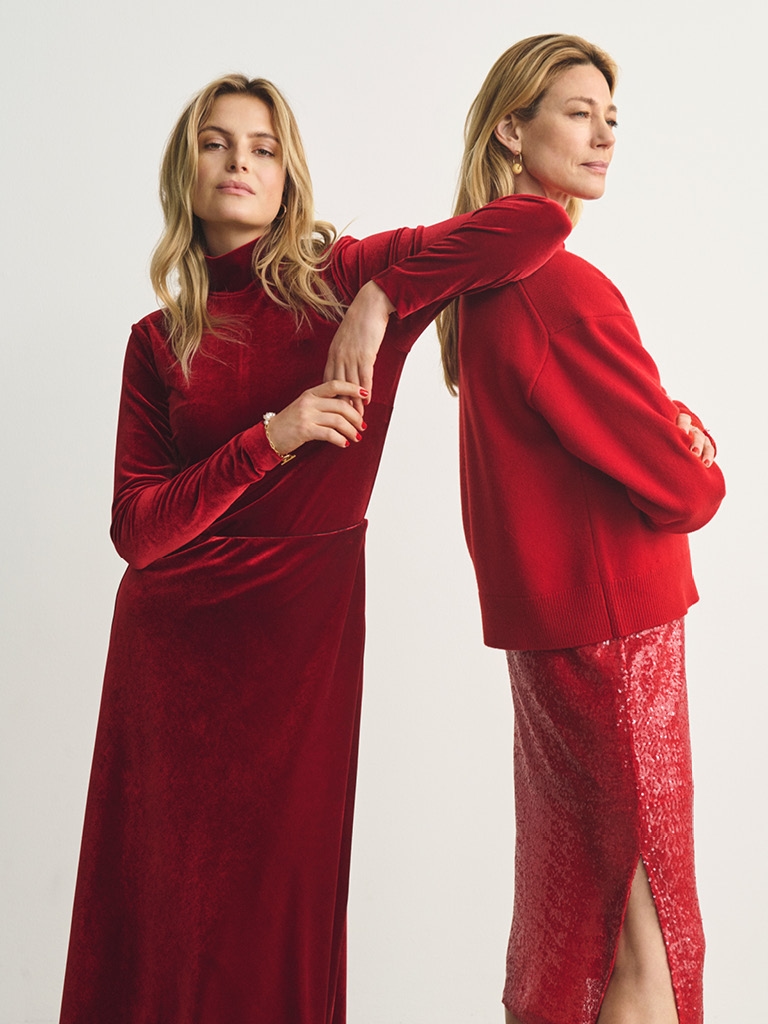 Two women standing with red coloured outfits. 